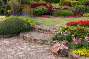 A winding stone path leads through lush greenery to a vibrant flower garden in full bloom.